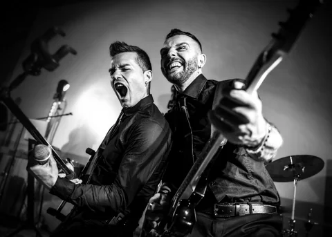 Black-and-white photo of The Gloves guitarist holding drumsticks beside the singer