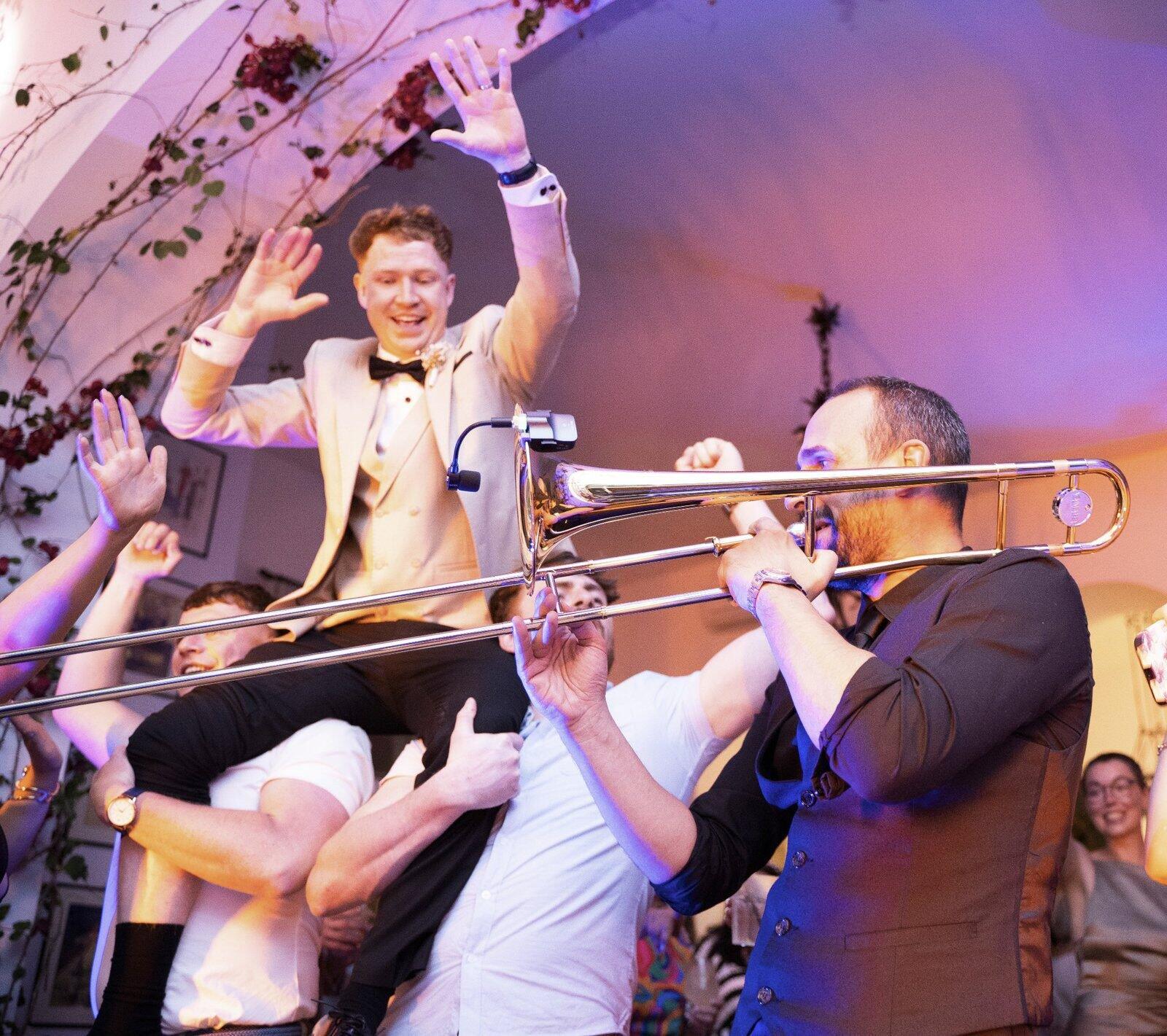 Sposo sollevato dagli amici mentre il trombone della band suona durante una festa di matrimonio in Italia